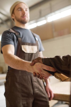 Photo for Young manual worker in overalls greeting his colleague at work shaking his hand - Royalty Free Image