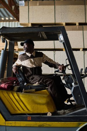 Téléchargez les photos : Chariot élévateur africain assis dans la chargeuse et conduisant pendant le travail à l'usine industrielle - en image libre de droit
