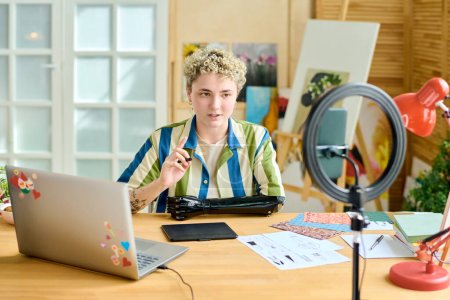 Junge selbstbewusste Bloggerin gibt Meisterkurs oder Training vor Online-Publikum, während sie zu Hause vor der Smartphone-Kamera sitzt