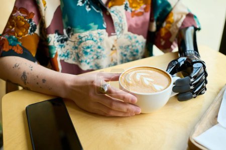 Téléchargez les photos : Mains de jeune femme avec bras partiel tenant tasse de cappuccino avec mousse de lait gonflée et décor créatif en forme de coeur en spirale - en image libre de droit