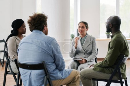 Photo for Young confident female psychologist in suit talking to group of intercultural people with psychological problems at session - Royalty Free Image