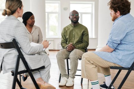 Foto de Uno de los pacientes interracial que describe su problema al psicólogo y otras personas mientras se sienta entre ellos durante la sesión en el consultorio - Imagen libre de derechos