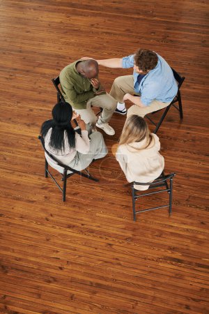 Photo for Above view of interracial people supporting African American man during session while attending course of psychological rehabilitation - Royalty Free Image