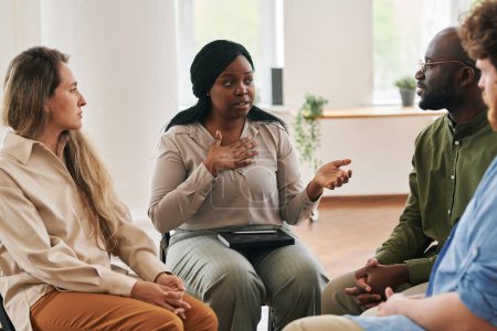 Foto de Mujer negra confiada describiendo su problema mental o preocupaciones a otras personas sentadas alrededor durante la sesión psicológica - Imagen libre de derechos