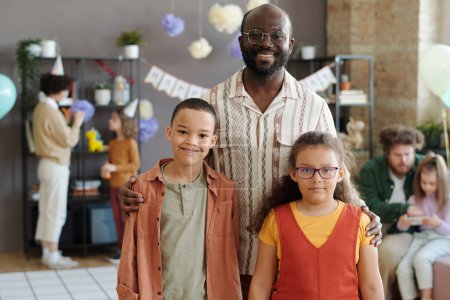 Téléchargez les photos : Portrait de famille afro-américaine de trois souriants à la caméra, heureux père posant avec ses deux enfants à la fête d'anniversaire - en image libre de droit