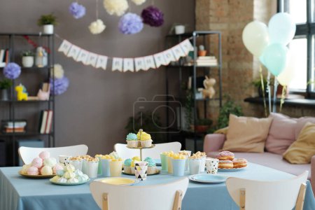 Téléchargez les photos : Image horizontale de barre de bonbons sur la table avec des cupcakes, des beignets, des bonbons se préparant pour la fête d'anniversaire à la maison - en image libre de droit