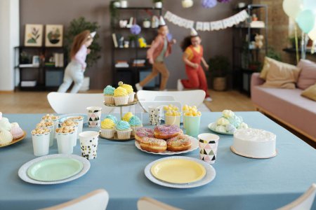 Foto de Imagen horizontal de la barra de caramelo en la mesa con rosquillas, magdalenas y palomitas de maíz con grupo de niños corriendo en segundo plano - Imagen libre de derechos