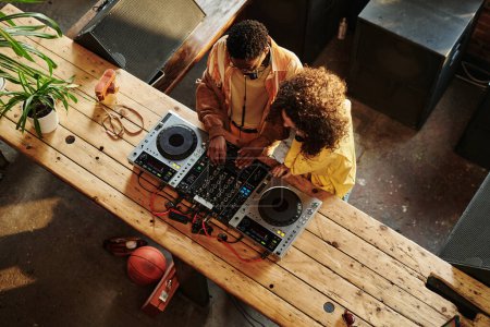 Téléchargez les photos : Au-dessus de la vue de jeune couple interculturel en casual création de nouvelles musiques tandis que le gars montrant à sa petite amie comment mélanger les sons - en image libre de droit