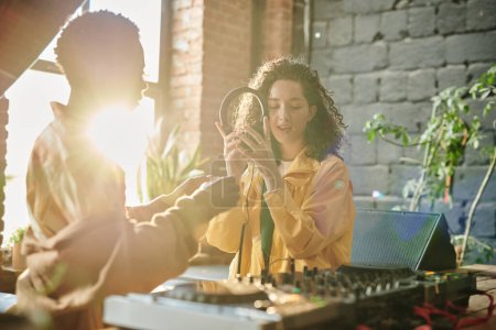 Téléchargez les photos : Jeune femme en tenue décontractée tenant des écouteurs tout en créant de la nouvelle musique avec son petit ami afro-américain dans l'appartement loft - en image libre de droit