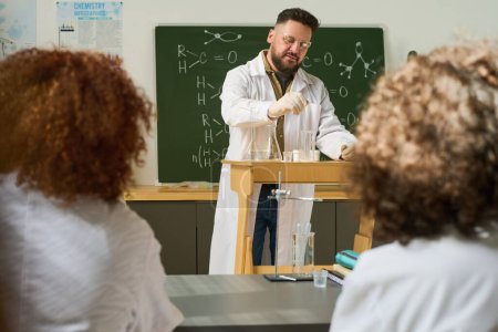 Photo for Mature male teacher of chemistry doing chemical experiment at lesson while standing in front of audience and dropping liquid into tube - Royalty Free Image
