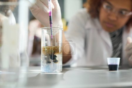 Photo for Female highschool student or researcher adding several drops of purple ink into glass containing transparent liquid chemical substance - Royalty Free Image