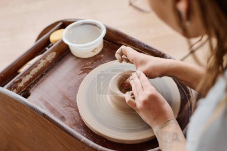 Téléchargez les photos : Mains de jeunes artisans ou potiers talentueux formant la partie supérieure d'un pot ou d'une cruche en terre cuite neuve tout en travaillant par roue de poterie en atelier - en image libre de droit