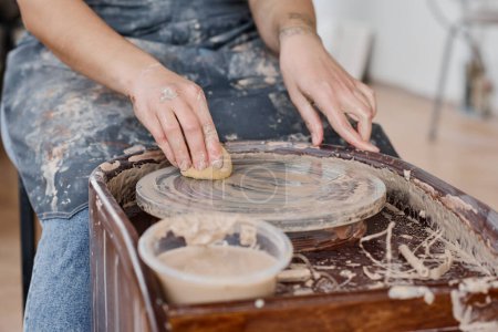Téléchargez les photos : Mains de jeune femme essuyant roue de poterie avec éponge humide après avoir créé de nouveaux articles en faïence à vendre en atelier ou en studio - en image libre de droit