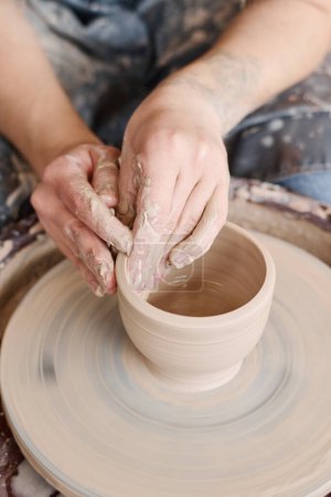 Foto de Manos de artesana creativa en el artículo de arcilla giratoria en la rueda de cerámica durante la creación de nuevos productos de barro para la venta en la tienda - Imagen libre de derechos