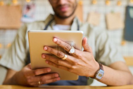 Téléchargez les photos : Mains de jeune homme noir tenant la tablette devant lui-même tout en réseautant et en regardant à travers les commandes en ligne de clients - en image libre de droit