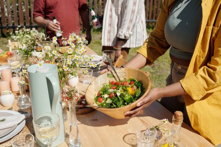 Photo for Young black woman serving table with homemade food, drinks, wildflowers and other stuff while waiting for guests - Royalty Free Image