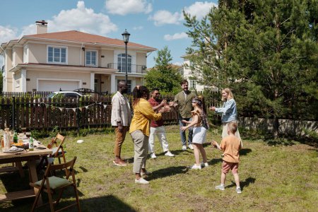 Foto de Grupo de jóvenes y felices hombres y mujeres interculturales aplaudiendo mientras juegan al escondite con los niños en el patio trasero de la casa de campo - Imagen libre de derechos