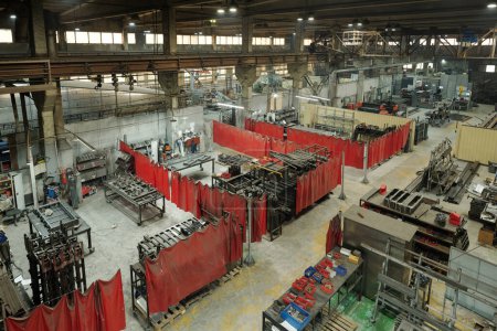 Foto de Cortinas rojas que dividen varios talleres con máquinas o partes del almacén con enormes piezas de repuesto metálicas entre sí - Imagen libre de derechos