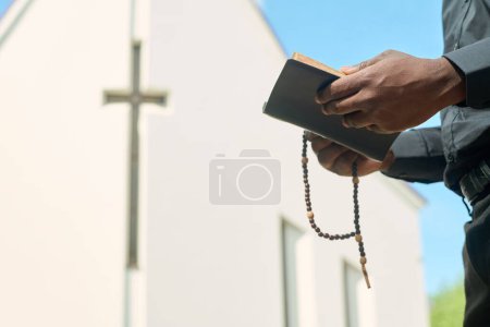 Foto de Manos de sacerdote en ropa negra sosteniendo cuentas de rosario y Evangelio abierto mientras lee versos y los explica durante el sermón - Imagen libre de derechos
