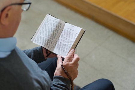 Foto de Por encima de tiro de hombre maduro en ropa de casualwear sosteniendo abierta la Santa Biblia mientras lee uno de los Evangelios durante el sermón en la iglesia - Imagen libre de derechos