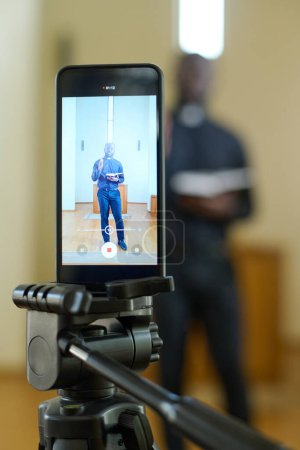 Photo for Screen of smartphone with pastor holding open Bible while standing in front of wooden pulpit and preaching during church service - Royalty Free Image