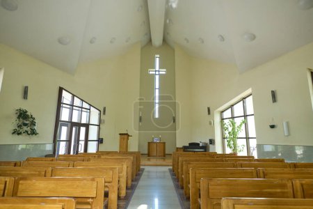 Foto de Salón vacío para los servicios de la iglesia con pasillo entre dos filas de bancos de madera para los feligreses y cruz sobre el púlpito del pastor - Imagen libre de derechos