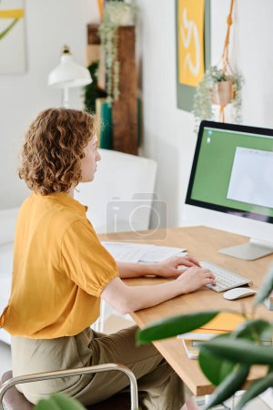 Téléchargez les photos : Jeune webdesigner freelance en casual avec ses mains sur le clavier en regardant le document électronique à l'écran de l'ordinateur - en image libre de droit