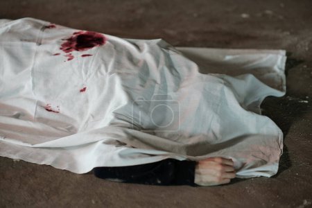Foto de Cadáver muerto de una persona muerta cubierta de sábana blanca yaciendo sobre asfalto en la escena del crimen en el área de estacionamiento o en algún otro lugar de la calle - Imagen libre de derechos
