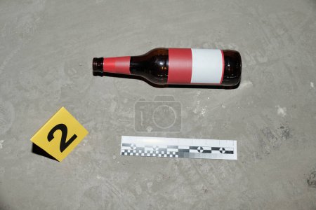 Téléchargez les photos : Plan ci-dessus de bouteille de bière vide avec autocollant vierge, carton jaune avec numéro de preuve et règle de l'enquêteur de scène de crime - en image libre de droit