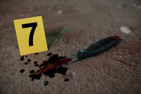 Téléchargez les photos : Gros plan du couteau représentant l'arme du crime avec des taches de sang de victime morte sur l'asphalte laissé par le criminel sur le lieu du meurtre - en image libre de droit