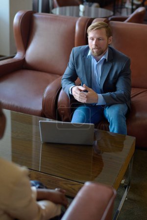 Photo for Young elegant entrepreneur in formalwear talking to foreign business partner sitting in front of him during discussion of working points - Royalty Free Image