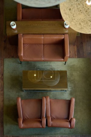 Photo for Above angle of brown leather sofa and two armchairs surrounding rectangular wooden table standing on grey carpet in hotel room - Royalty Free Image
