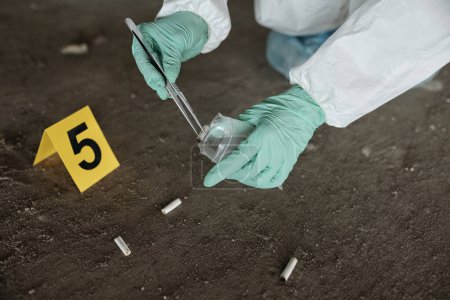 Foto de Guantes manos de experto criminológico con pinzas metálicas poniendo tocones de cigarrillos en el paquete de plástico durante la inspección de evidencias - Imagen libre de derechos