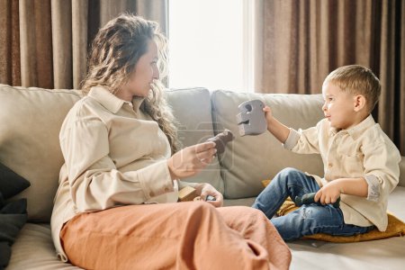 Photo for Young woman with long blond wavy hair playing with toy animals with her cute little son and helping him learn their names - Royalty Free Image