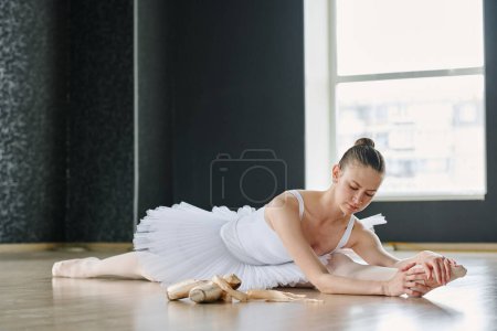 Téléchargez les photos : Jeune femme gracieuse attrayante se penchant vers l'avant sur la jambe tendue tout en étant assis dans la ficelle sur le sol pendant l'exercice chorégraphique - en image libre de droit