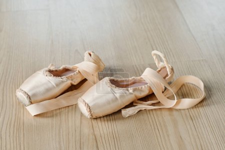 Foto de Par de nuevos zapatos puntiagudos desatados de color beige con cintas de seda en el suelo de salón de baile o aula para repeticiones de ejercicios de ballet - Imagen libre de derechos