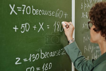 Photo for Young college teacher writing down equation on blackboard at lesson while preparing for explanation of new subject to students - Royalty Free Image