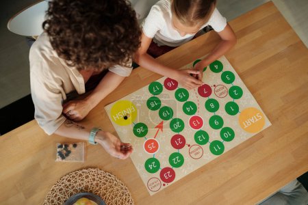 Foto de Por encima del ángulo de la mujer joven tirando dados sobre papel con círculos rojos y verdes que contienen números mientras juega juego de ocio - Imagen libre de derechos