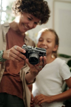 Photo for Hands of young woman holding photocamera and showing new photos to her youthful daughter after shooting at leisure - Royalty Free Image