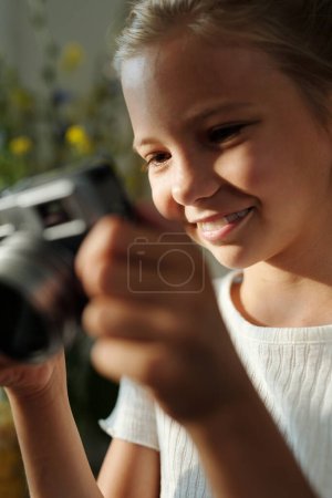 Téléchargez les photos : Souriante jeune fille avec appareil photo regardant à travers de nouvelles photos et appréciant tout et tout le monde autour d'elle - en image libre de droit