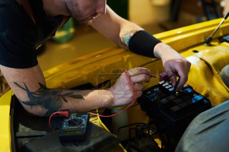 Photo for Hands of young technician bending over motor of car and using multimeter while testing new equipment after repairing - Royalty Free Image