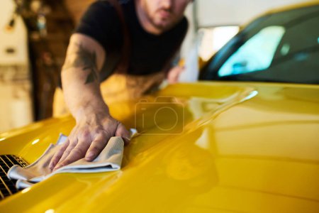 Photo for Hand of young male technician with duster wiping surface of yellow car body while cleaning cover of hood after repairment - Royalty Free Image