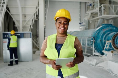 Photo for Happy young African American woman with tablet standing in front of camera in production plant or workshop and networking - Royalty Free Image
