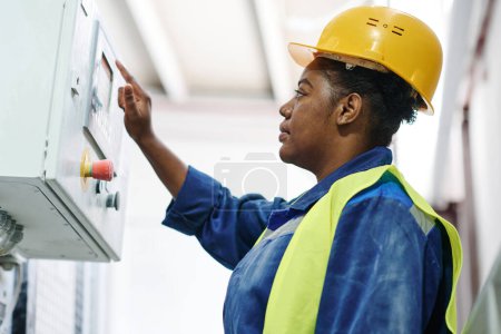 Photo for Young serious African American female engineer pressing button on panel to start machinery equipment during work in factory - Royalty Free Image