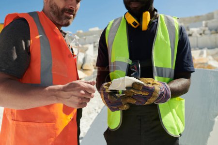 Photo for Mid section of two intercultural workers of marble quarry in uniform discussing sort of solid rock while one of them holding its part - Royalty Free Image