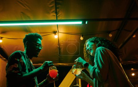 Photo for Happy young multicultural dates in casualwear having chat and cocktails while cheerful girl laughing during talk with boyfriend - Royalty Free Image