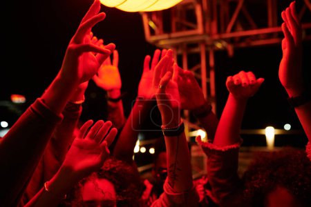 Téléchargez les photos : Les mains levées de jeunes amis énergiques dansant à la fête sur le toit dans un café en plein air la nuit et appréciant leur rassemblement - en image libre de droit