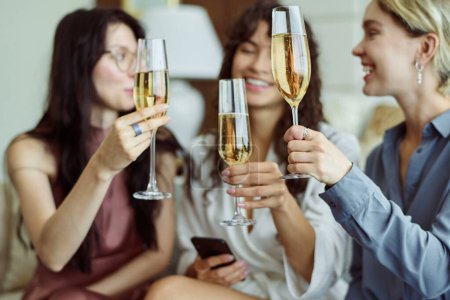 Photo for Three happy girls with champagne celebrating forthcoming wedding of one of them while holding flutes and making toast at hen party - Royalty Free Image
