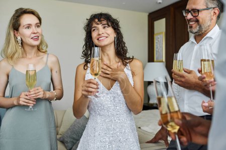Téléchargez les photos : Groupe de personnes gaies avec des flûtes de champagne griller à la fête de mariage tout en écoutant jolie mariée en robe blanche magnifique - en image libre de droit
