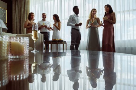 Téléchargez les photos : Deux petits groupes d'invités de mariage ou des membres de la famille de la mariée avec champagne debout devant la table dans le salon à la fête - en image libre de droit